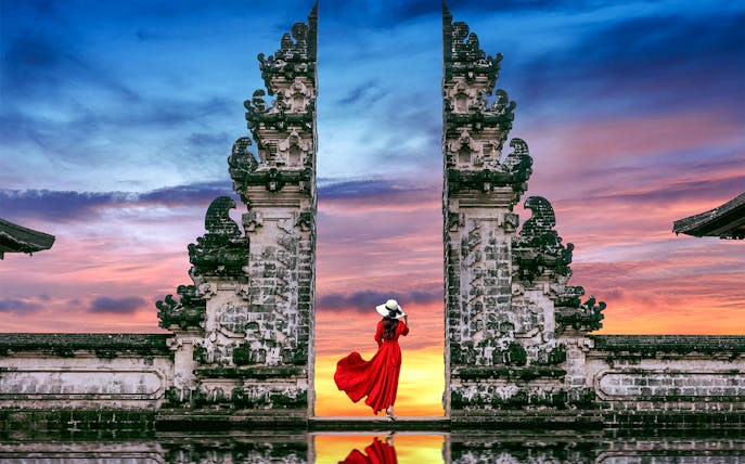 Woman in red dress at Bali's Lempuyang Temple gates during sunrise.