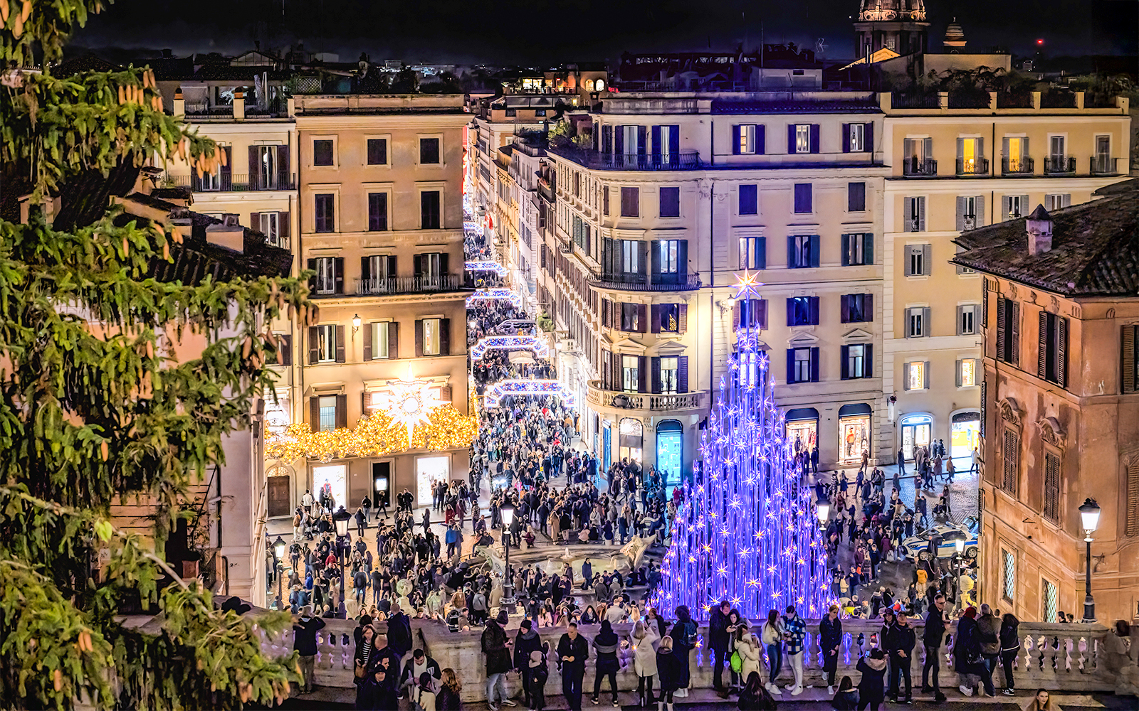 Via Condotti leading to Piazza di Spagna with festive Christmas lights and a large illuminated tree.
