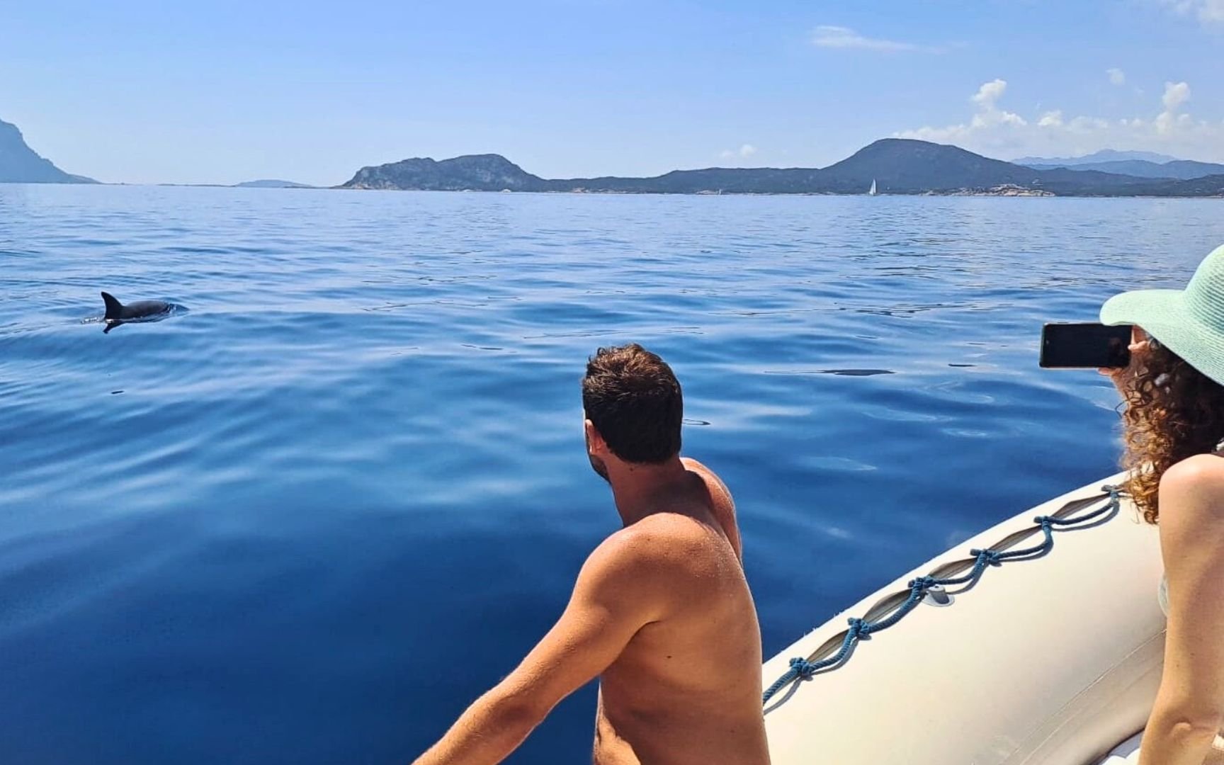 Tourists on a boat watching a dolphin near Capo Figari, Sardinia.