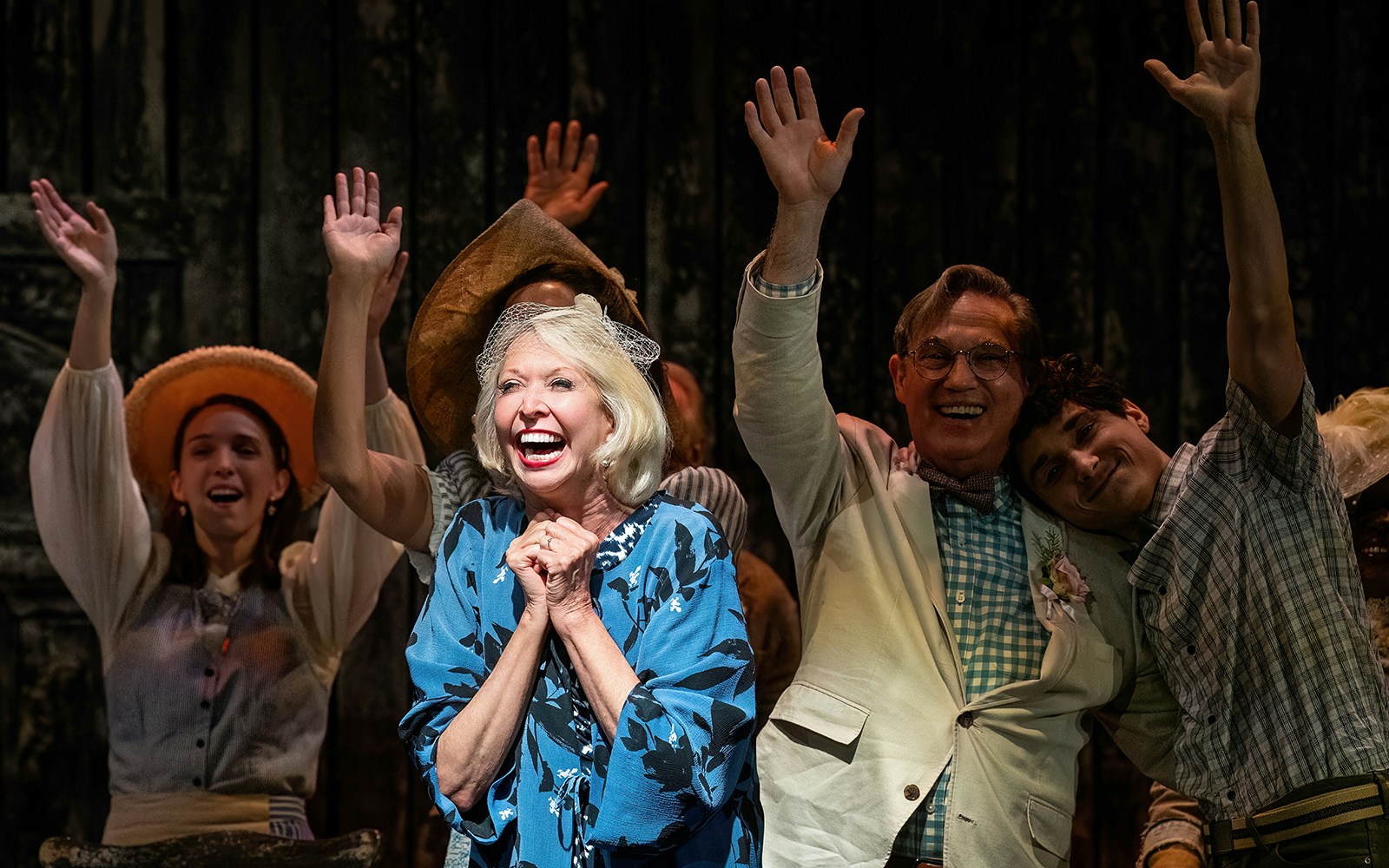 Cast members of "Our Town" on stage, smiling and waving during a performance.