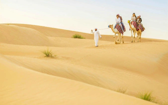 Camel ride through Dubai desert dunes during safari tour.