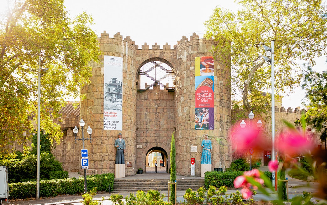 Entrance to Poble Espanyol in Barcelona with stone archway and colorful banners.