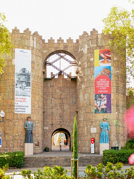 Entrance to Poble Espanyol in Barcelona with stone archway and colorful banners.