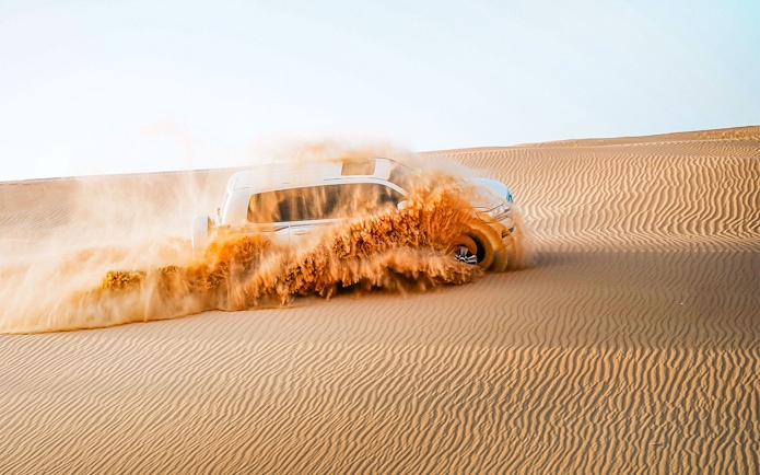 SUV driving through sand dunes in Abu Dhabi desert.