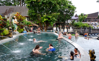 Visitors enjoying a hot spring pool surrounded by statues and lush greenery in Indonesia.