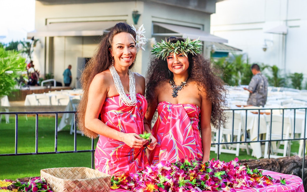 Women in traditional Hawaiian attire preparing leis at Moana Luau, Hawaii.