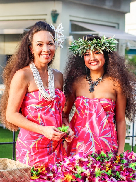 Women in traditional Hawaiian attire preparing leis at Moana Luau, Hawaii.