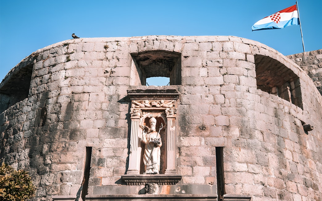 Dubrovnik city wall with statue and Croatian flag, Game of Thrones tour location.