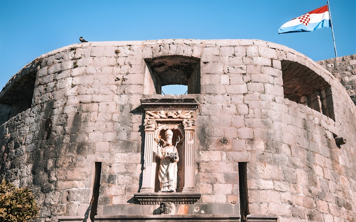 Dubrovnik city wall with statue and Croatian flag, Game of Thrones tour location.