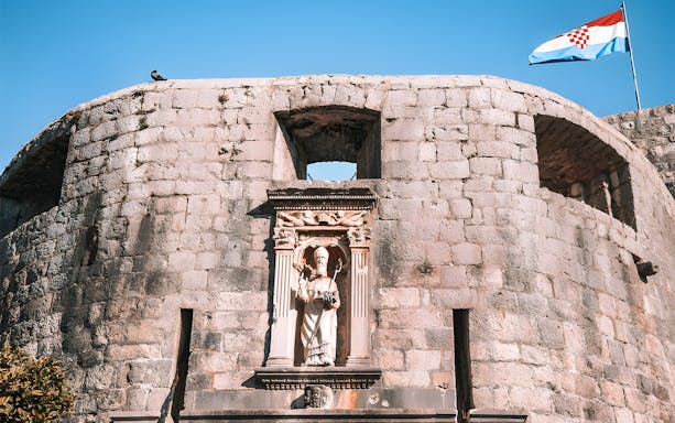Dubrovnik city wall with statue and Croatian flag, Game of Thrones tour location.