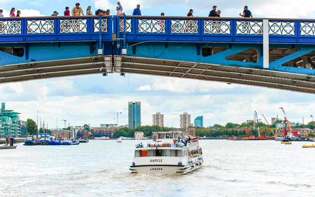 Sightseeing boat on Thames River passing under a bridge in London.