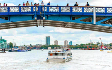 Sightseeing boat on Thames River passing under a bridge in London.