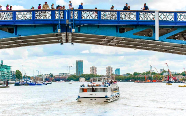 Sightseeing boat on Thames River passing under a bridge in London.