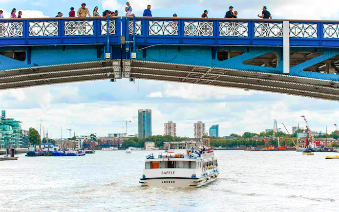 Sightseeing boat on Thames River passing under a bridge in London.