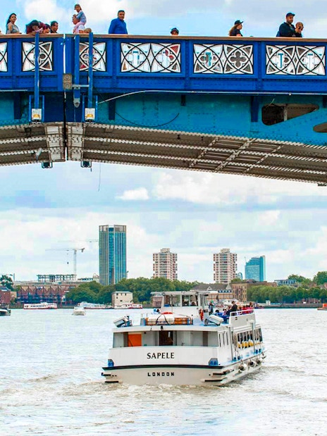 Sightseeing boat on Thames River passing under a bridge in London.