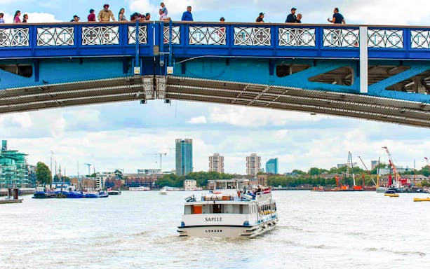 Sightseeing boat on Thames River passing under a bridge in London.