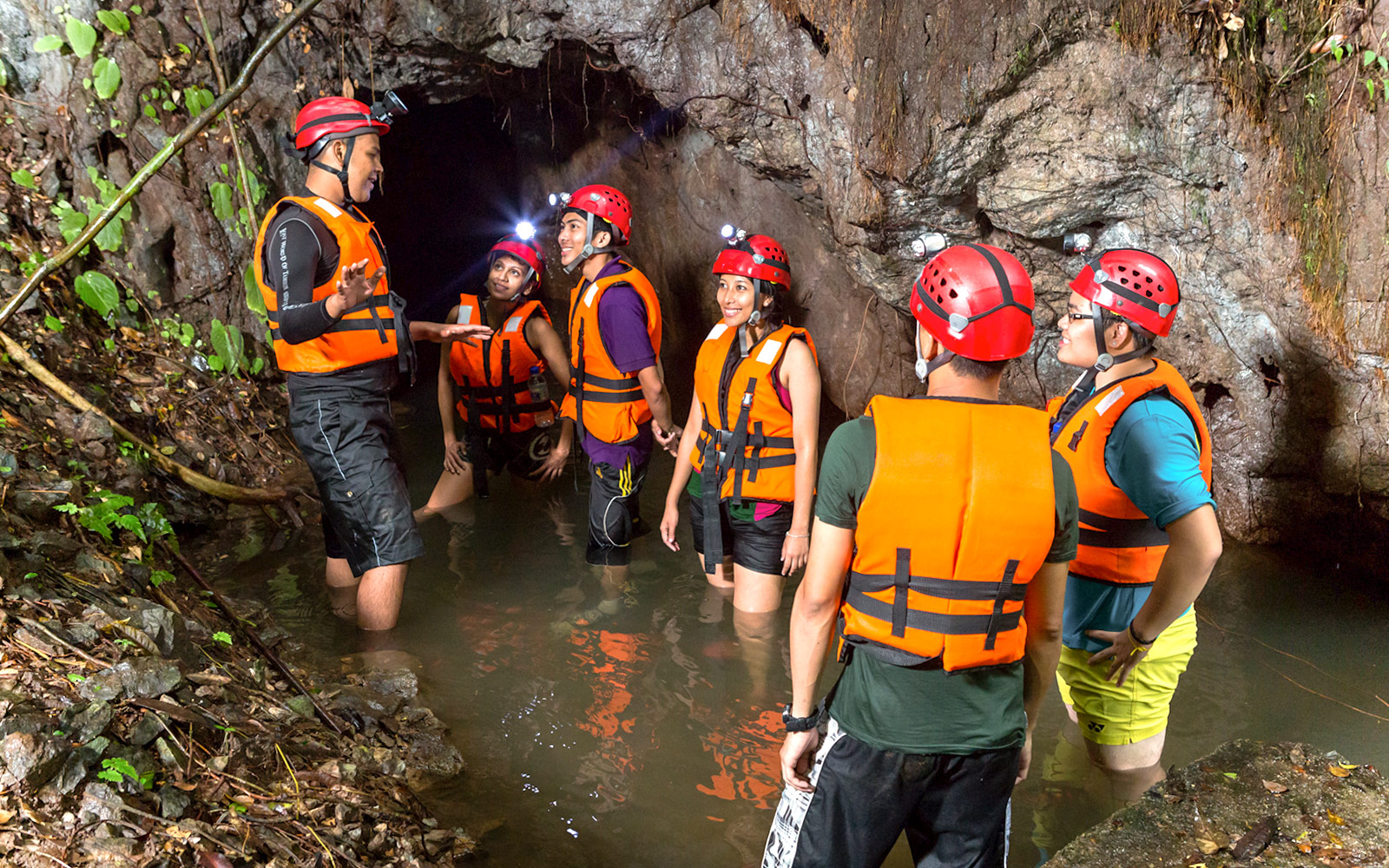 Group exploring cave in water at Sunway Lost World of Tambun, Malaysia, wearing helmets and life vests.