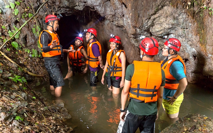 Group exploring cave in water at Sunway Lost World of Tambun, Malaysia, wearing helmets and life vests.