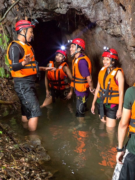 Group exploring cave in water at Sunway Lost World of Tambun, Malaysia, wearing helmets and life vests.