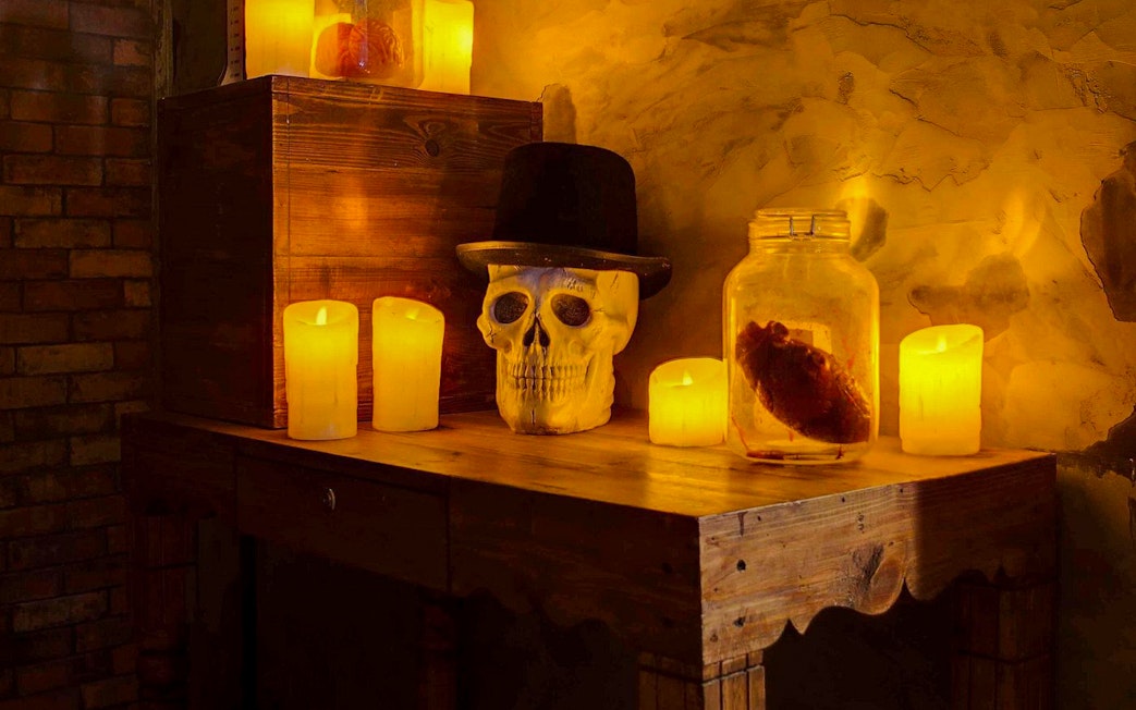 Skull with hat and candles on a wooden table in Jack The Ripper Escape Room, Dubai.