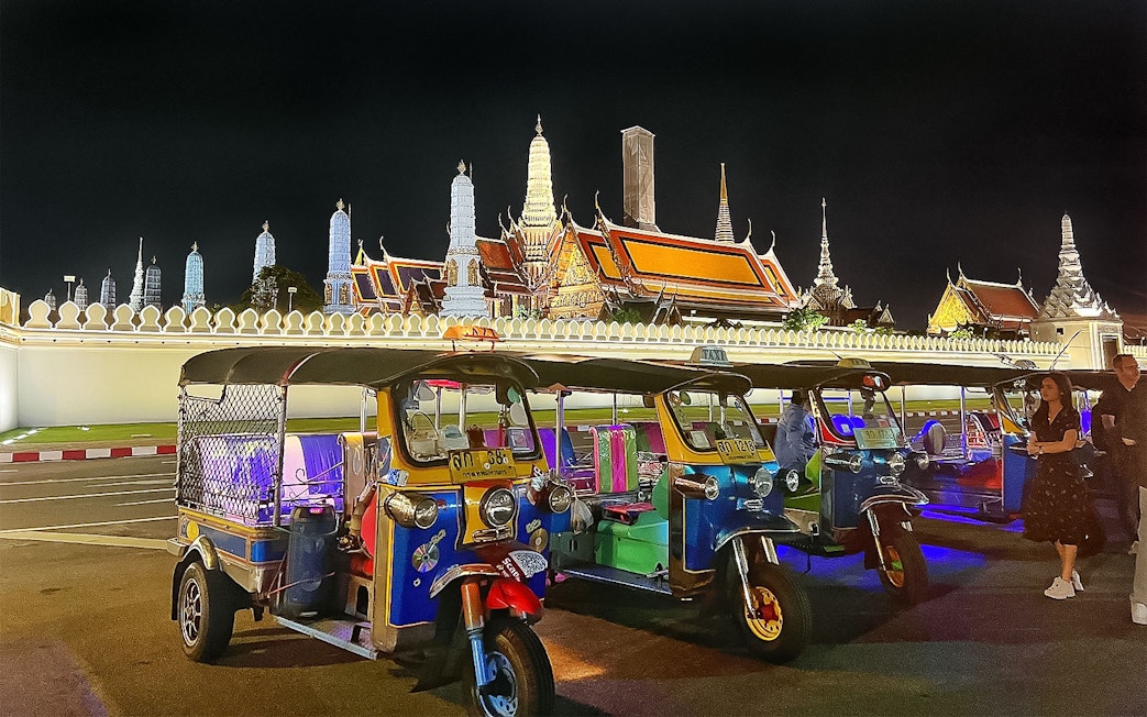 Tuk-tuks parked in front of Bangkok's Grand Palace at night during a guided tour.