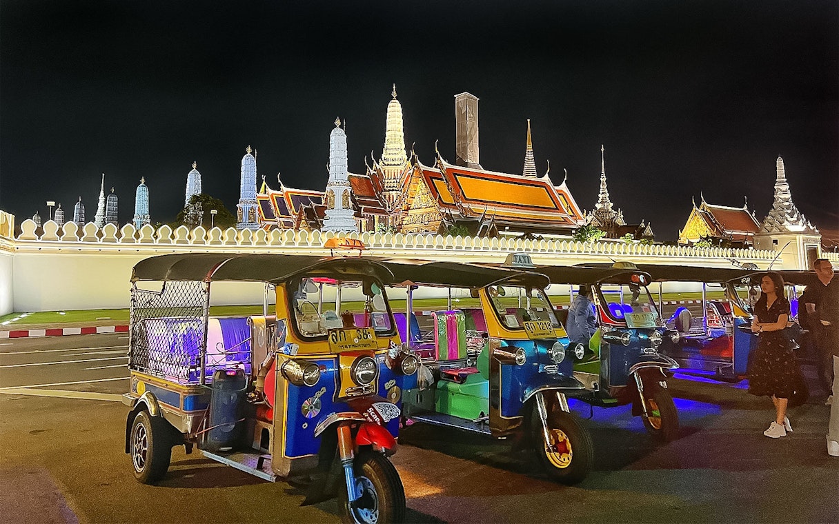 Tuk-tuks parked in front of Bangkok's Grand Palace at night during a guided tour.
