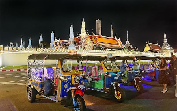 Tuk-tuks parked in front of Bangkok's Grand Palace at night during a guided tour.
