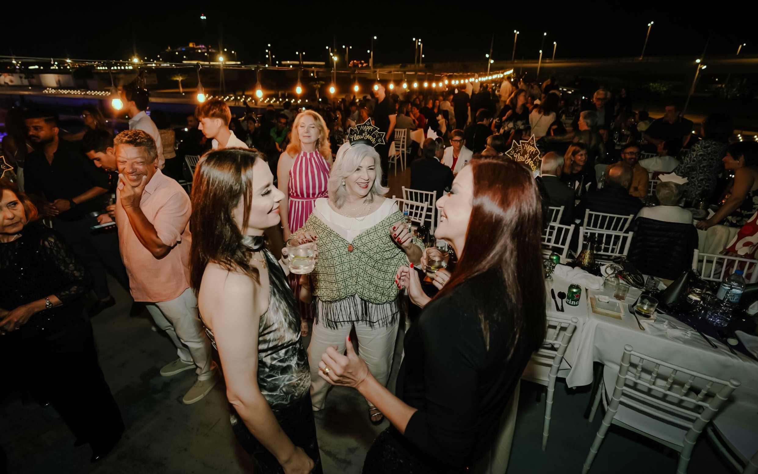 Guests enjoying New Year's Eve on a Marina Dhow dinner cruise, with festive lights and drinks.