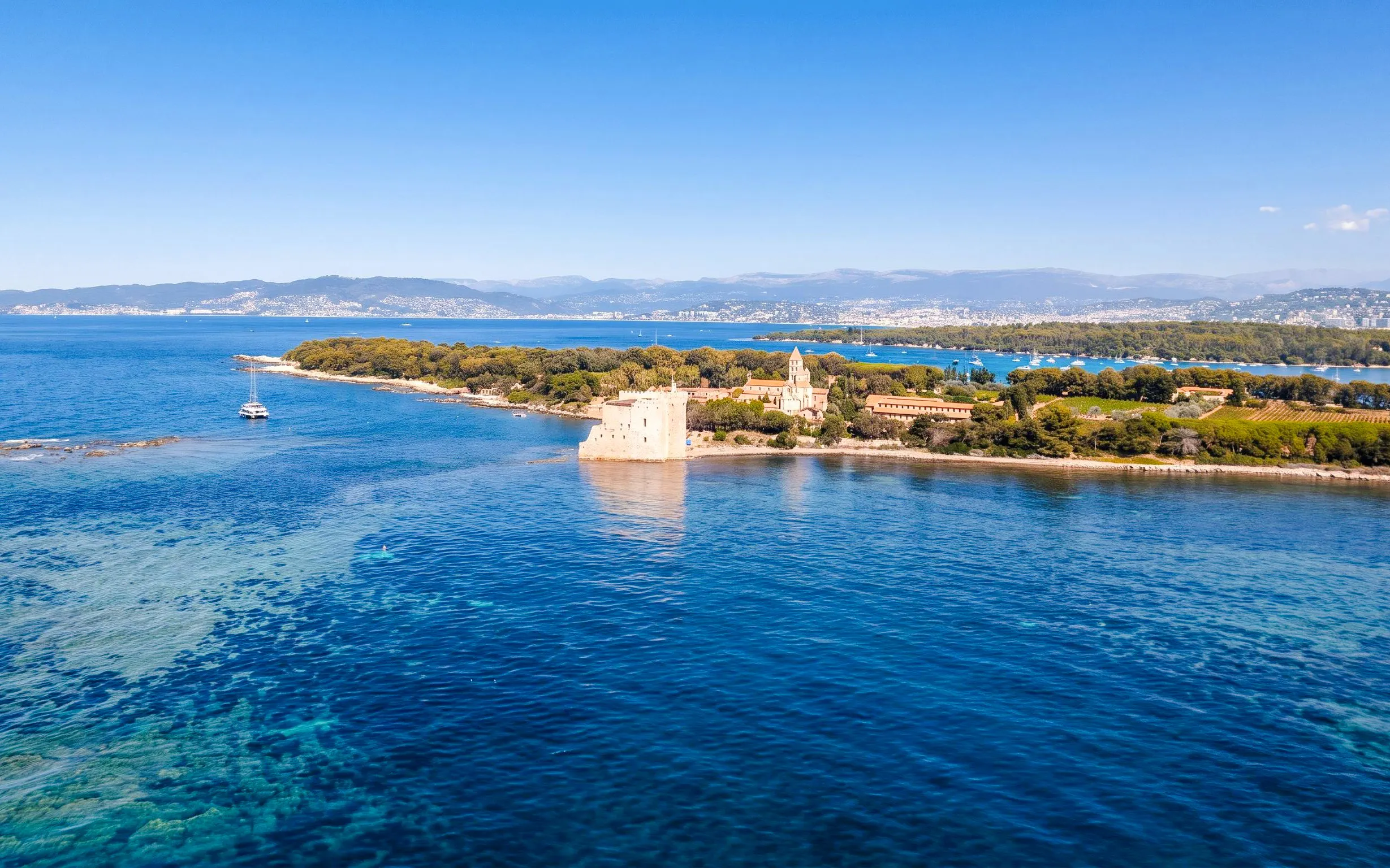 Catamaran near Lérins Island with historic fort and lush landscape, Marina Bay of Angels.