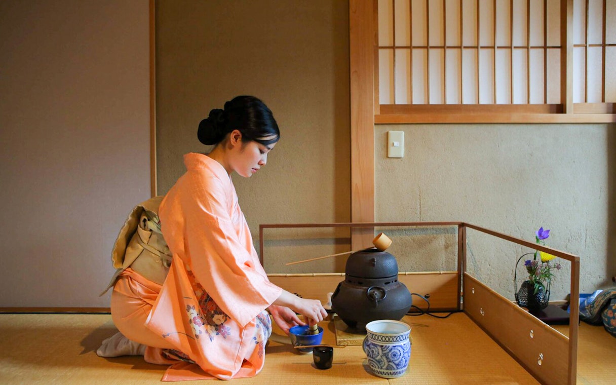 Tea ceremony in Kyoto teahouse with woman in kimono preparing tea.