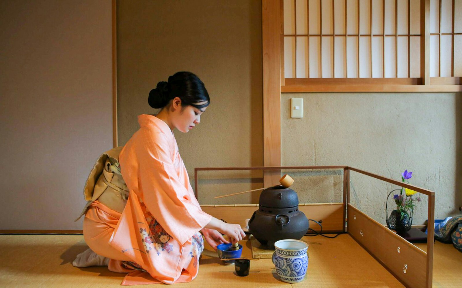 Tea ceremony in Kyoto teahouse with woman in kimono preparing tea.