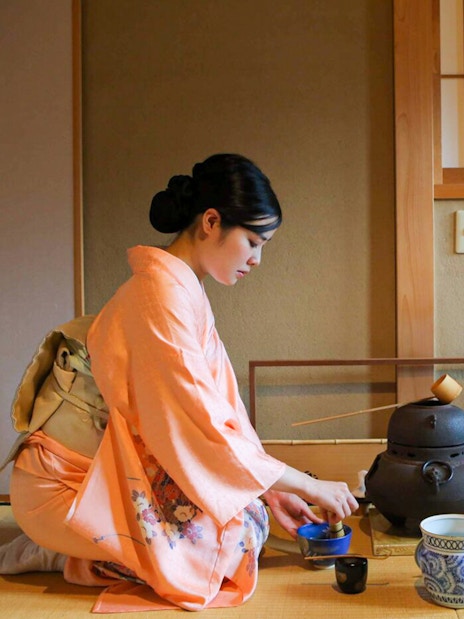 Tea ceremony in Kyoto teahouse with woman in kimono preparing tea.