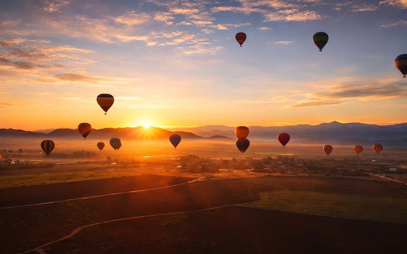 Hot air balloons at sunrise over Marrakech landscape.