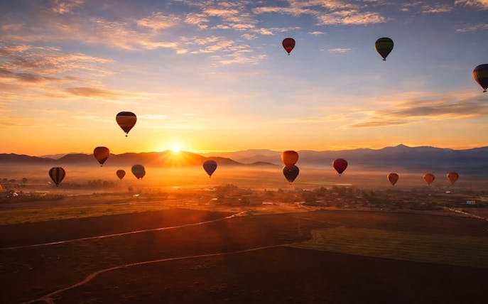 Hot air balloons at sunrise over Marrakech landscape.
