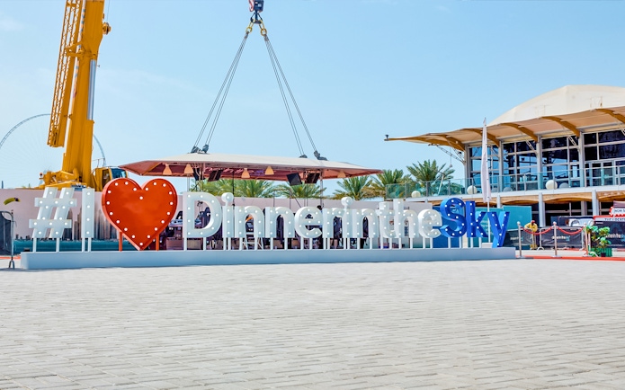 Dinner in the Sky sign with crane and dining platform in outdoor setting.