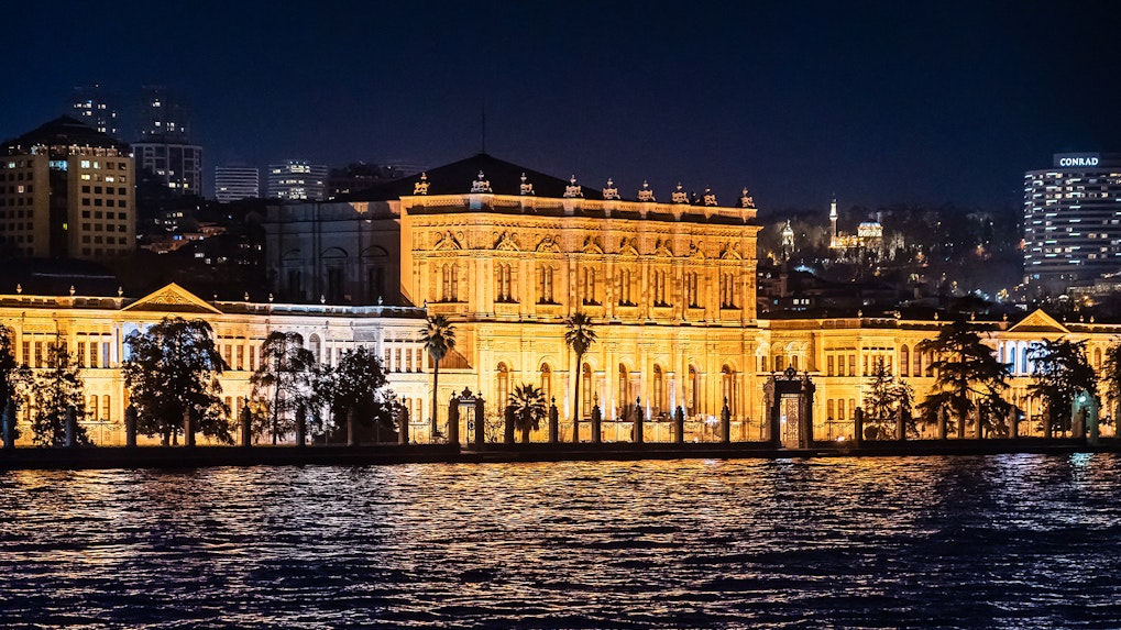 Illuminated Dolmabahçe Palace waterfront façade at night, Istanbul.