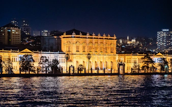 Illuminated Dolmabahçe Palace waterfront façade at night, Istanbul.