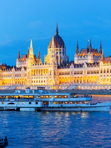 Cruise ship on Danube River with Budapest Parliament illuminated at dusk.