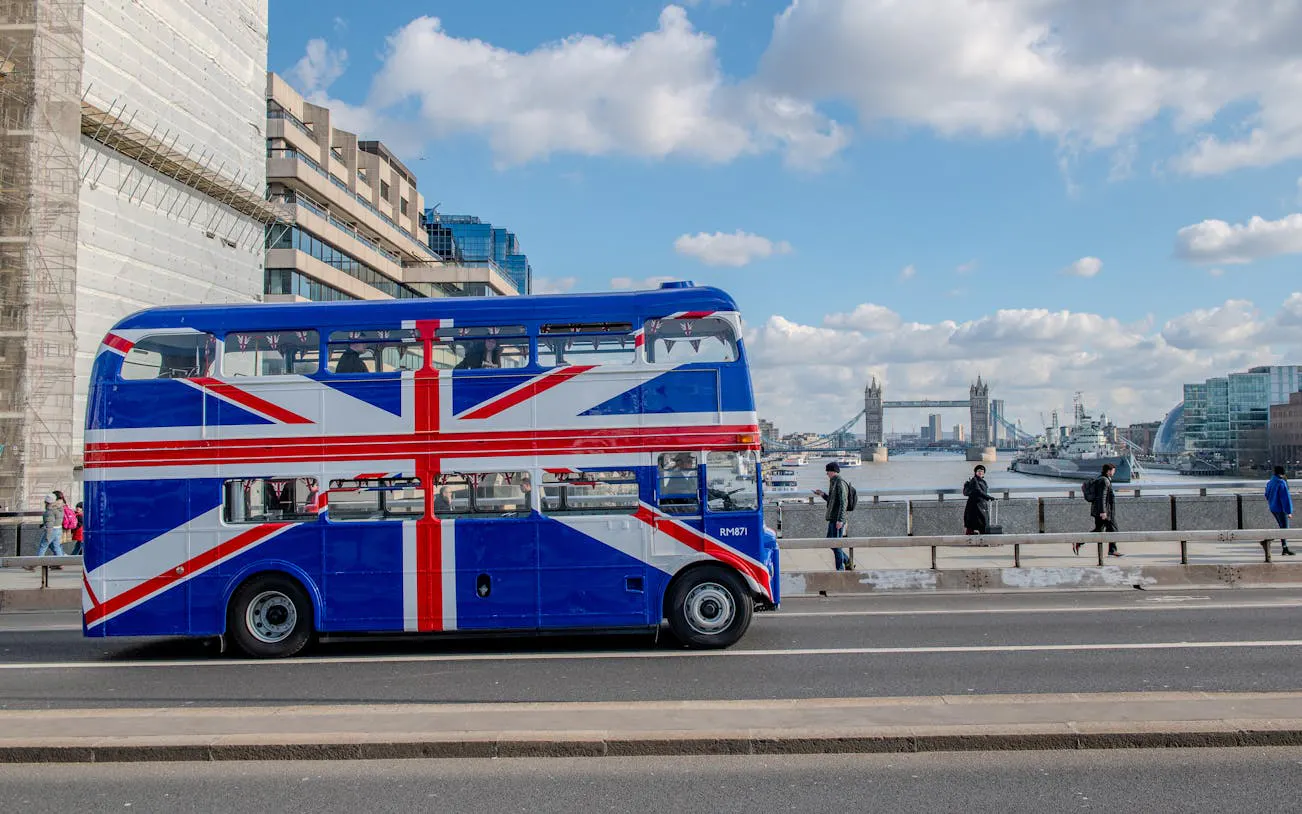 Double-decker bus with Union Jack design on London Bridge, Tower Bridge in background.