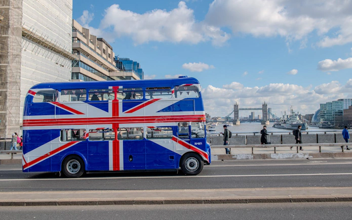 Double-decker bus with Union Jack design on London Bridge, Tower Bridge in background.