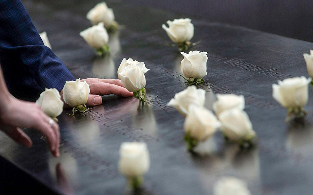 Hands touching engraved names with white roses at 9/11 Memorial, New York City.