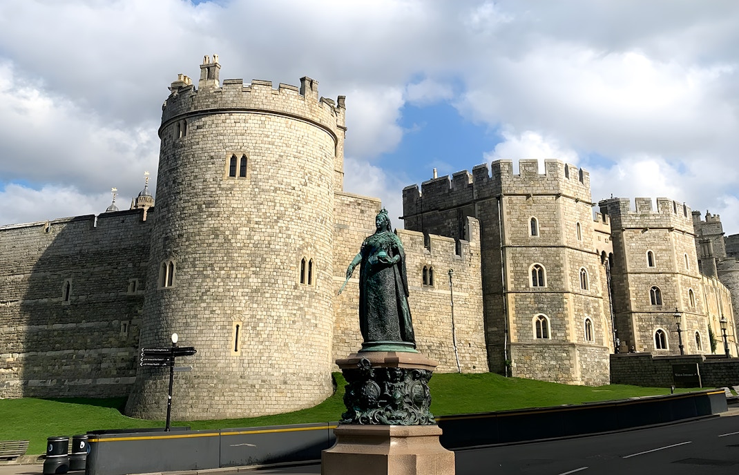 Windsor Castle with a statue in the foreground under a cloudy sky.
