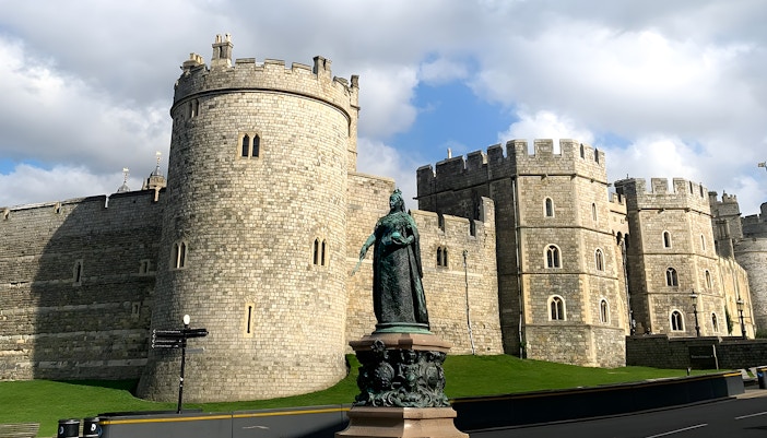 Windsor Castle with a statue in the foreground under a cloudy sky.