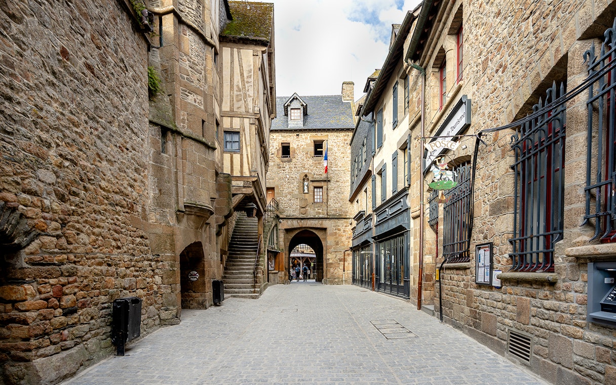 Mont Saint-Michel stone street with historic buildings and archway, France.