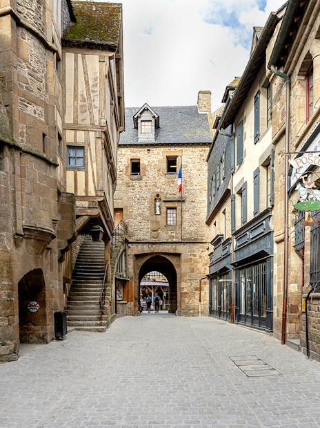 Mont Saint-Michel stone street with historic buildings and archway, France.