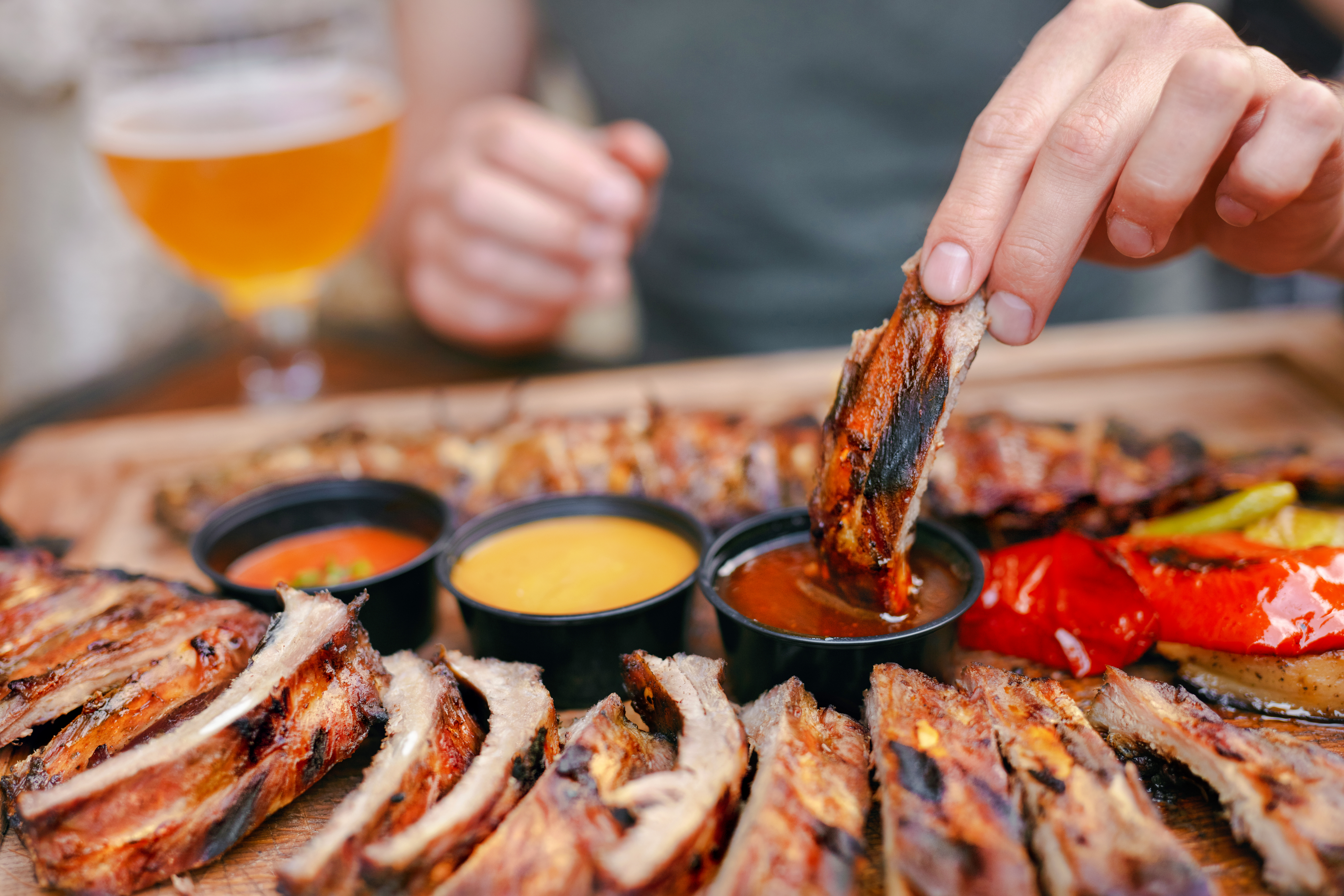 Barbecue ribs with sauces on a wooden platter in a rustic setting.