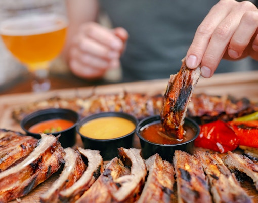 Barbecue ribs with dipping sauces and grilled vegetables on a wooden platter.