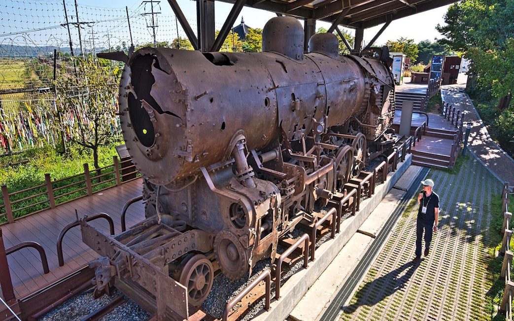 Rusty locomotive at DMZ, South Korea, with barbed wire fence and colorful ribbons in the background.