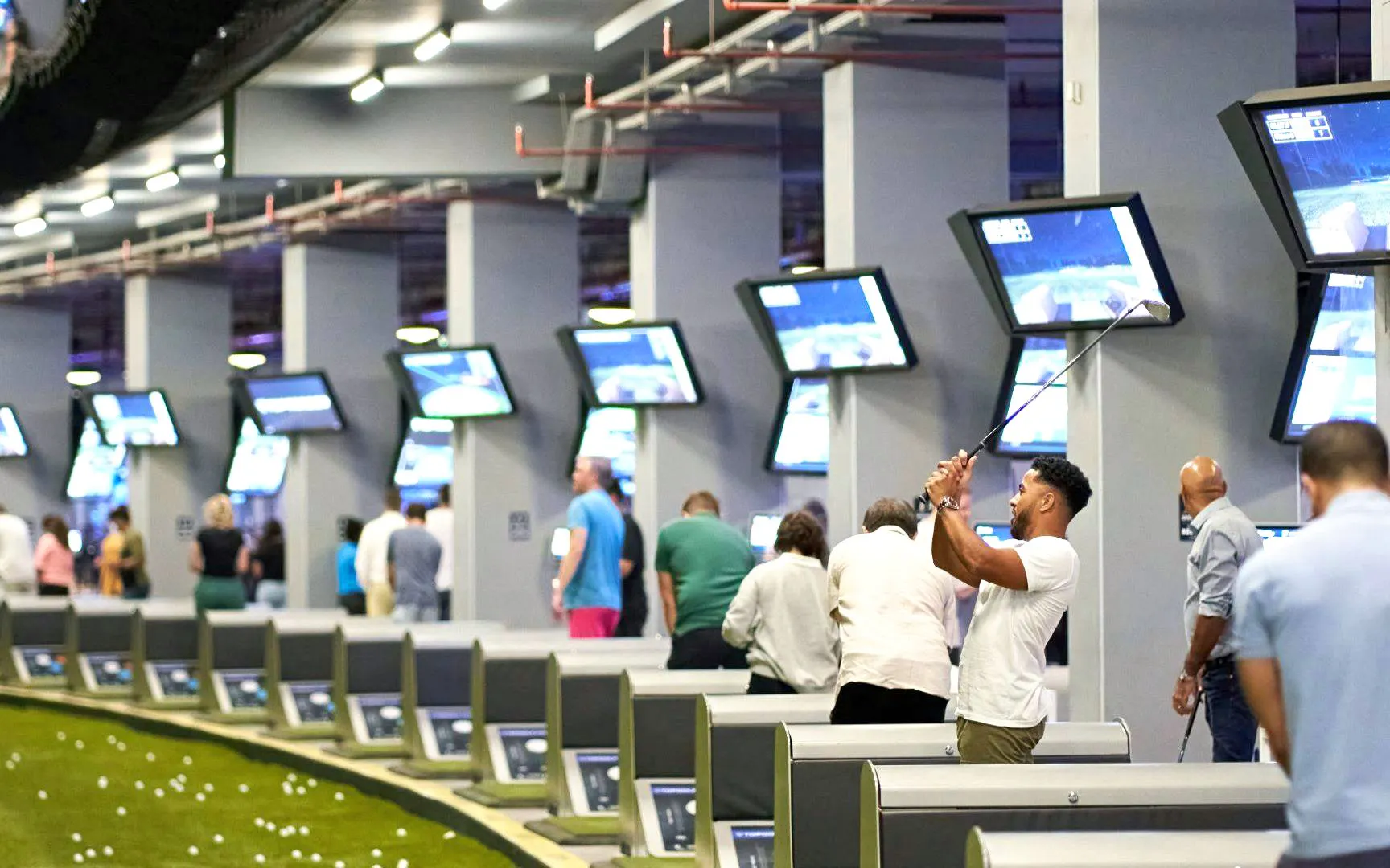 Golfers playing at indoor batting cages, TopGolf Dubai.