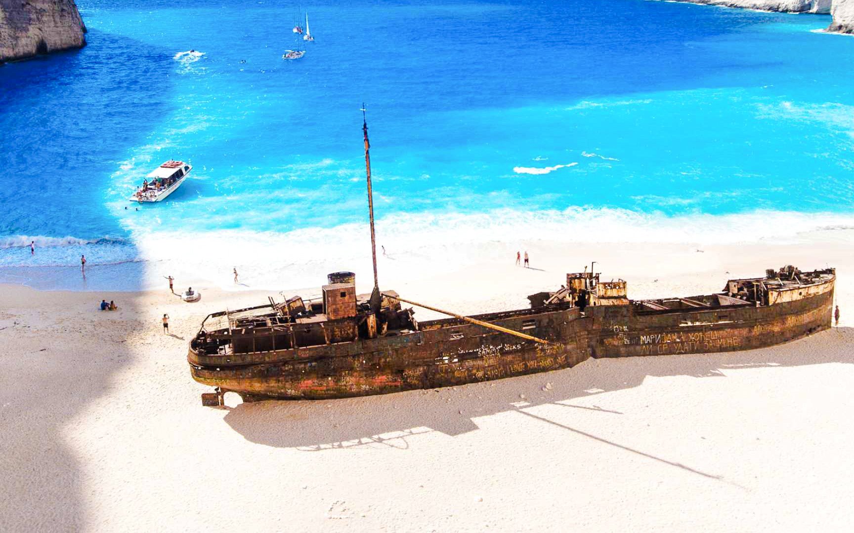 Shipwreck on Navagio Beach, Zante with tourists and boats in the turquoise water.